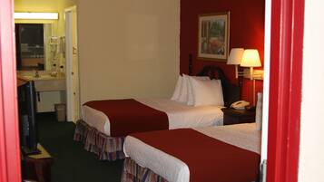 A hotel room with two beds, a desk, a chair, a mirror, a painting on the wall, and a lamp.