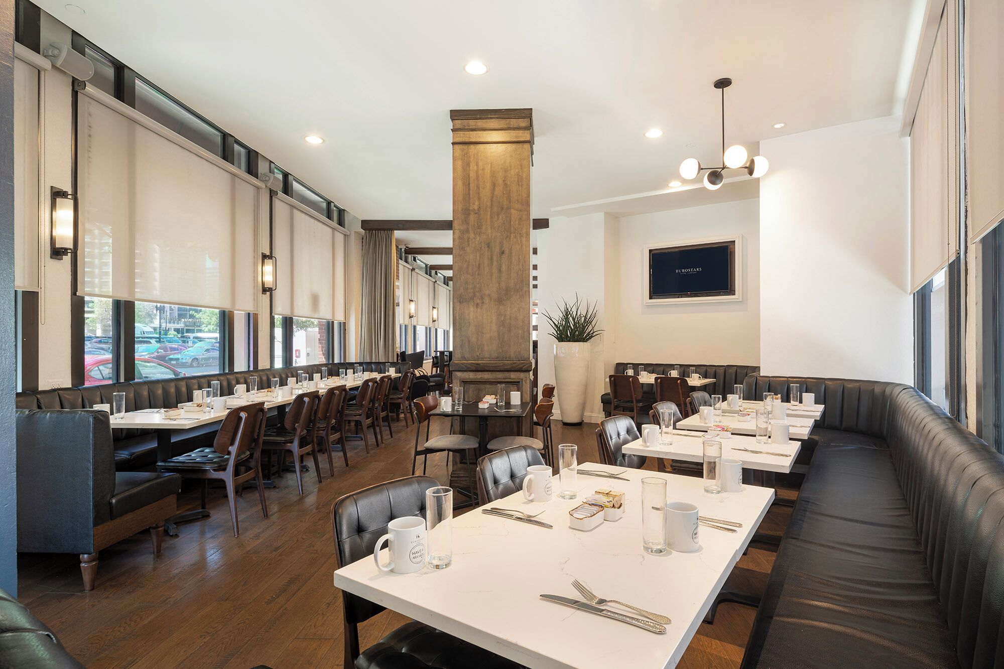 Een restaurant met meerdere eettafels en zitgedeeltes, grote ramen en een modern interieur.