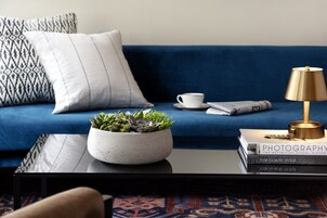 A modern living room with a blue sofa, a white cushion, a coffee cup, a book titled 'Photography', and a small potted plant on a black table.
