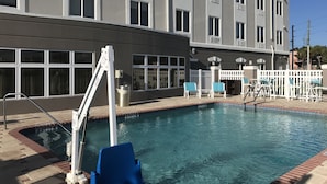 Una piscina con un puesto de salvavidas, una valla blanca y un edificio con varias ventanas al fondo.