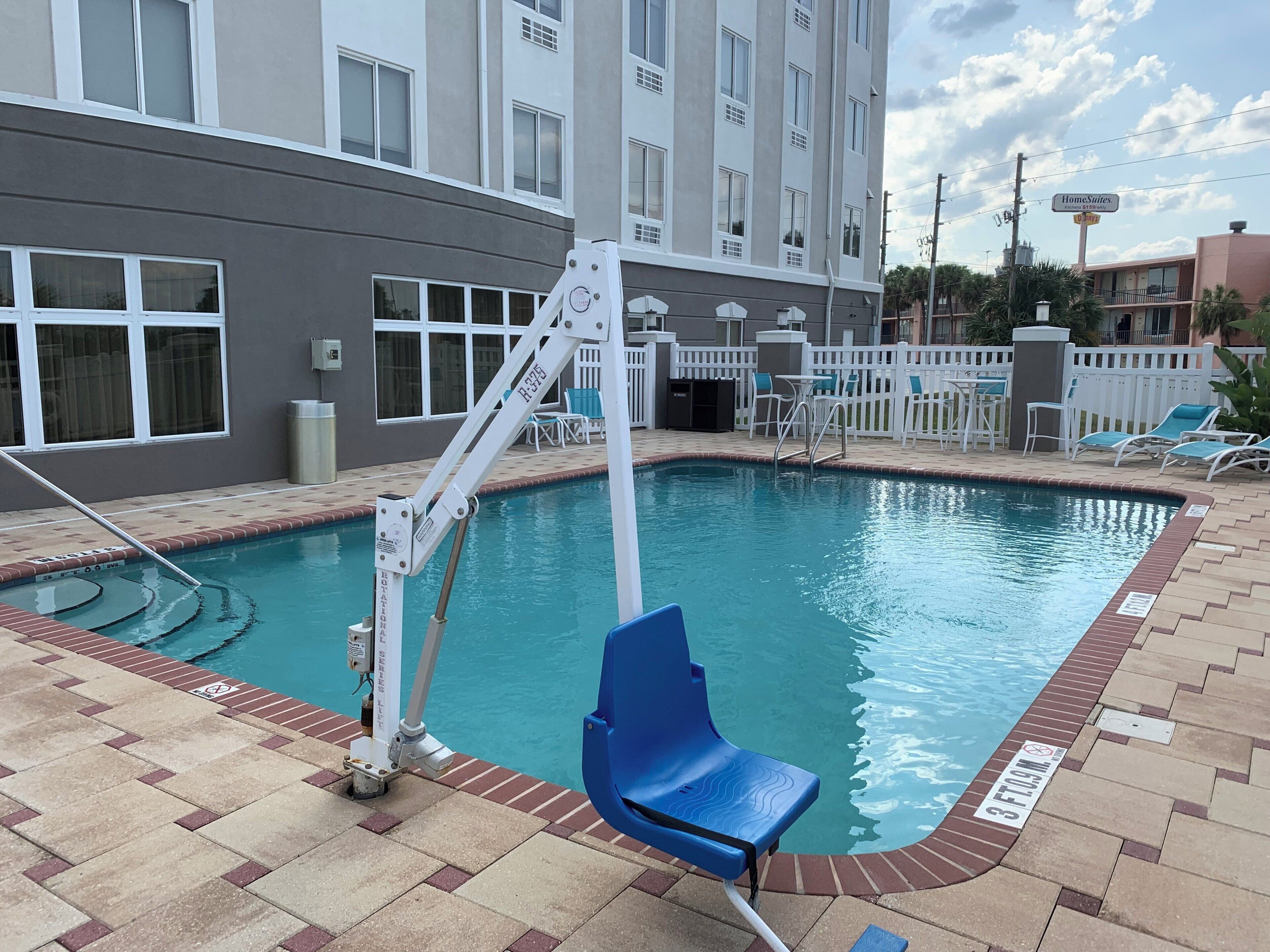 A swimming pool with a pool lift, a lounge chair, and a fenced patio area.
