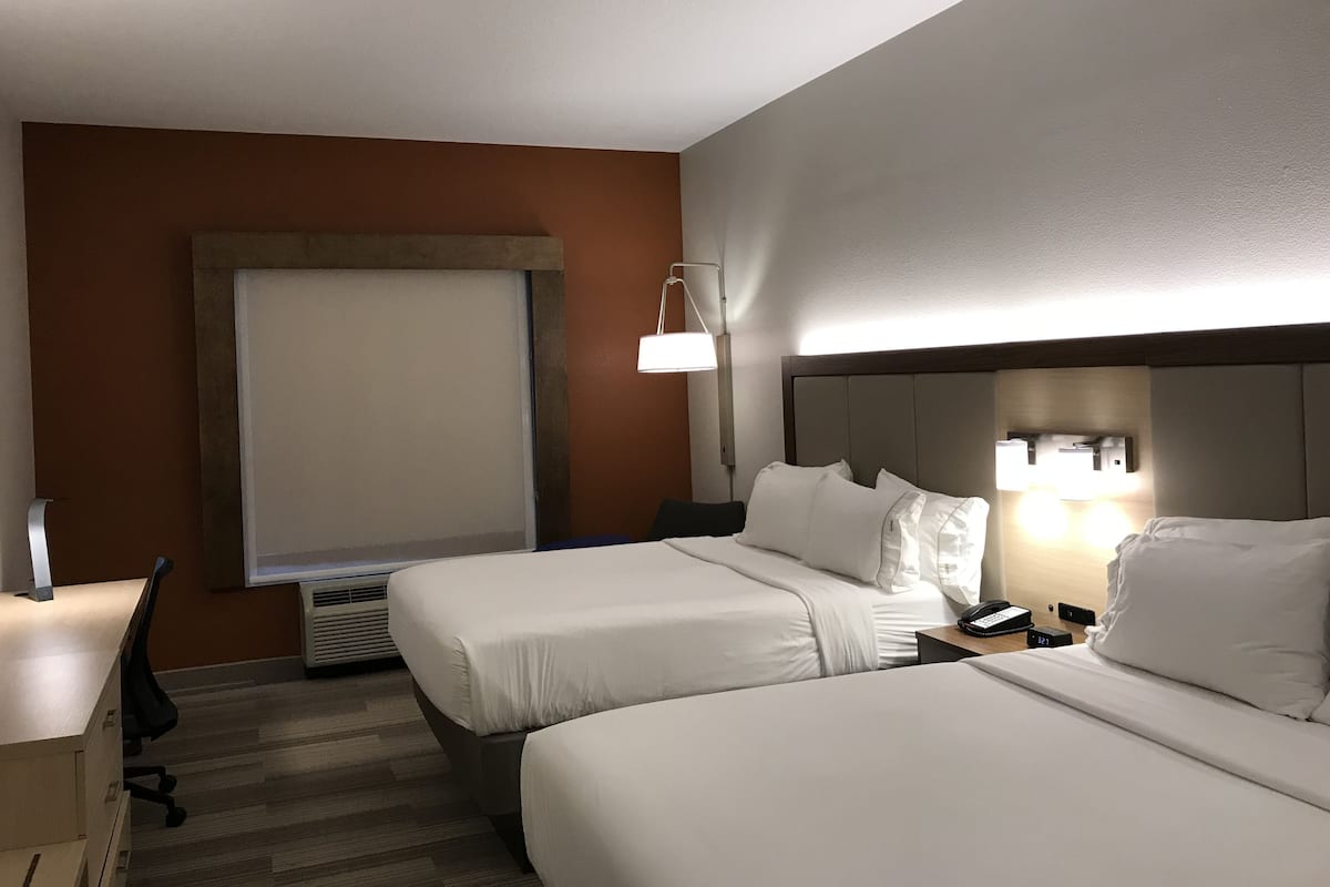 Ett hotellrum med två sängar, ett skrivbord, en stol, en lampa och ett fönster.