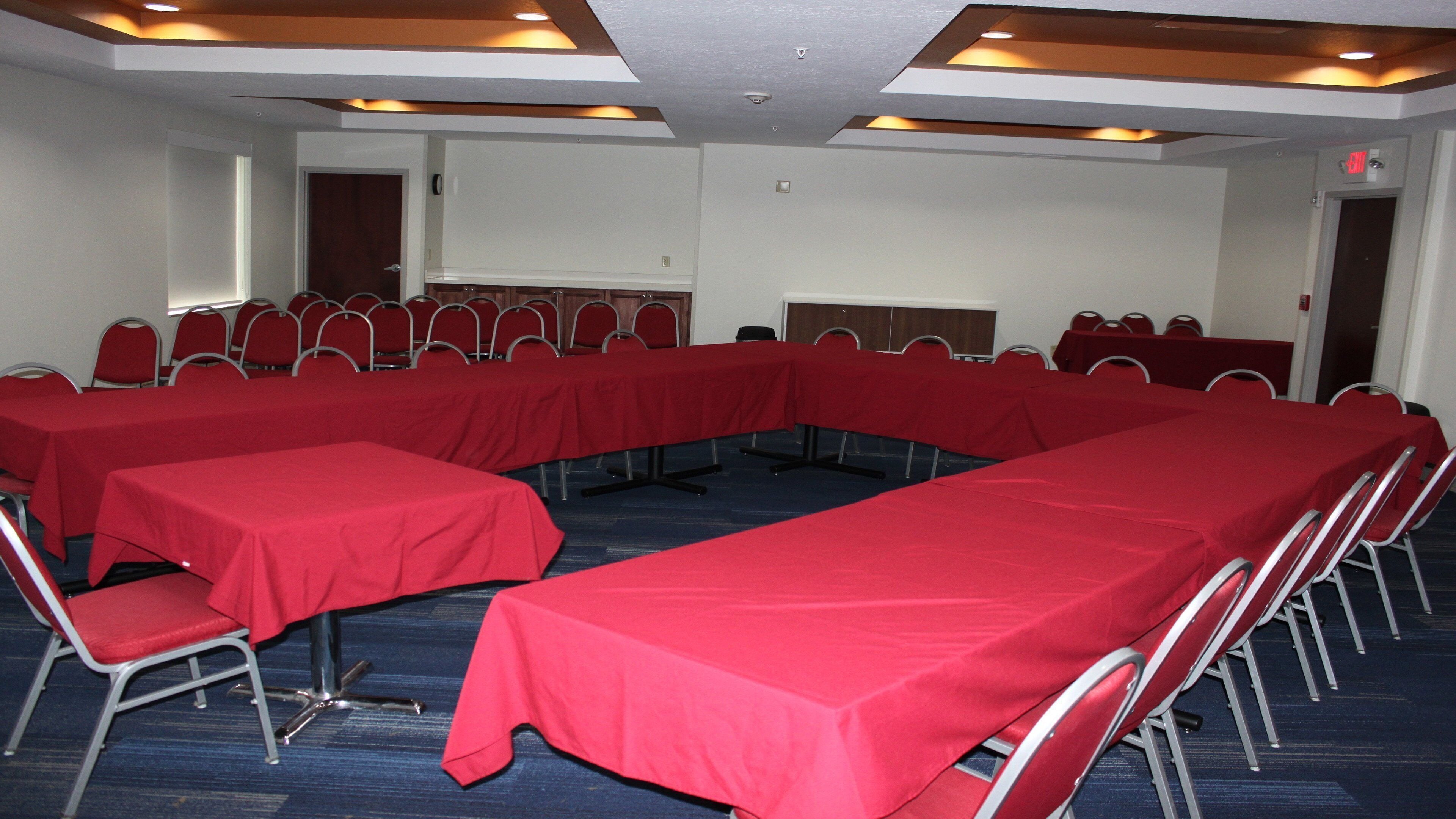 Une salle de conférence dotée de plusieurs tables et chaises, disposées en forme de U.
