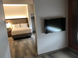 Camera d'albergo con un letto, un comodino con una lampada, una televisione a schermo piatto montata a parete e un pavimento rivestito di moquette.