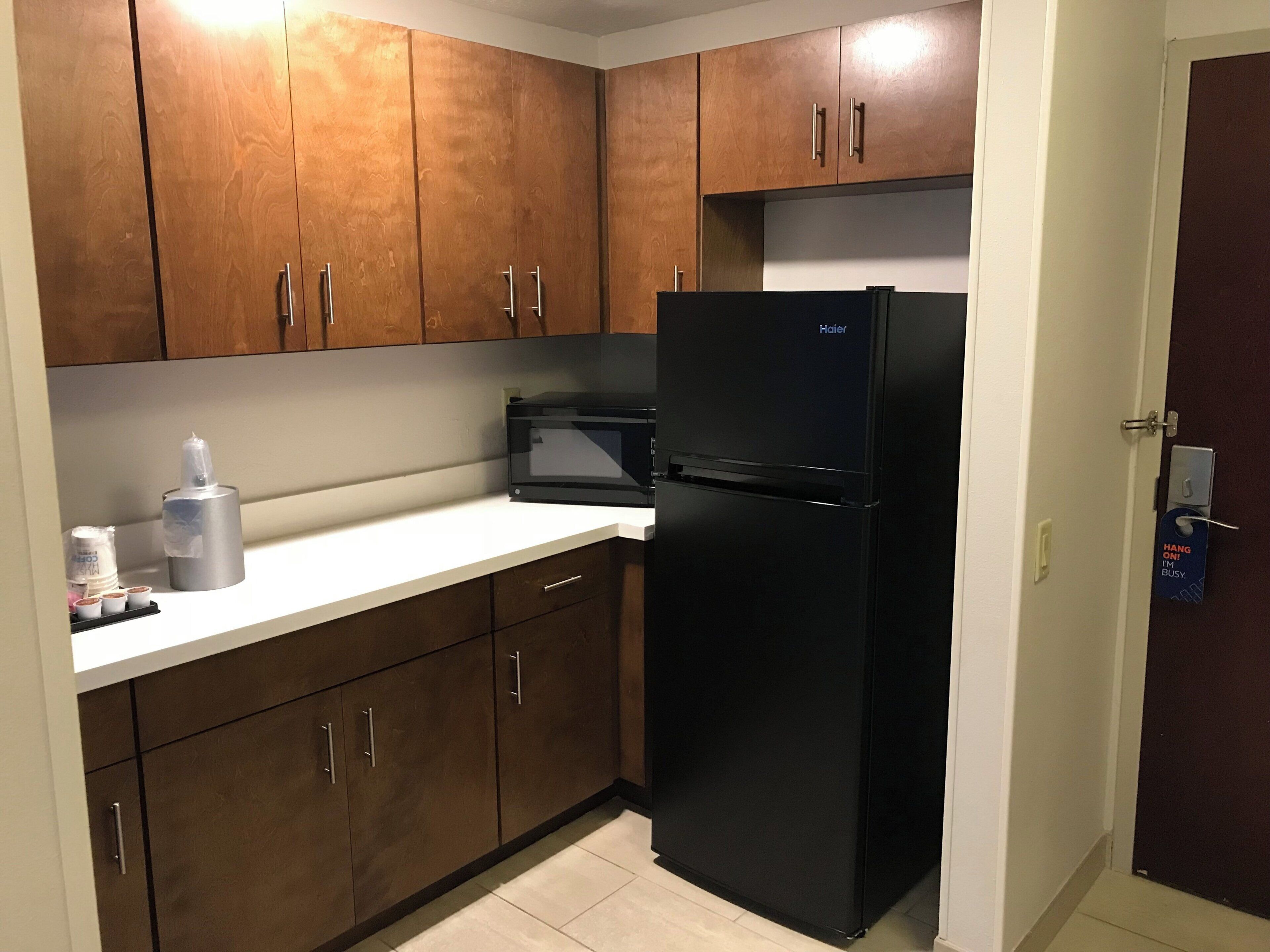 Una cocina compacta con armarios de madera, un refrigerador negro y un microondas.