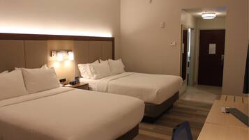 A hotel room with two beds, a desk, and a chair. There is a nightstand with a clock and a lamp.