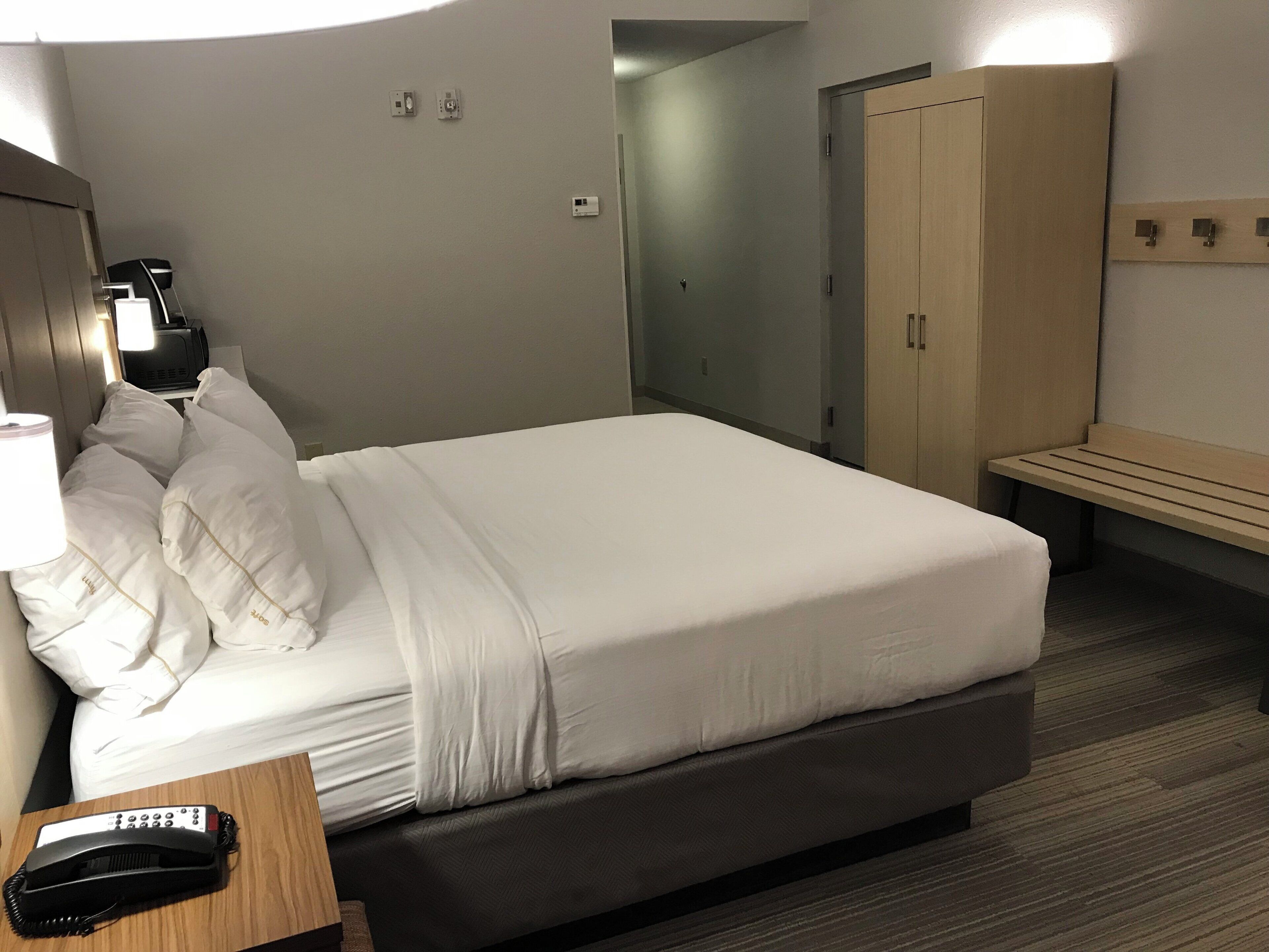 Ein Hotelzimmer mit Bett, Nachttischtelefon, Lampe und einer hölzernen Bank.