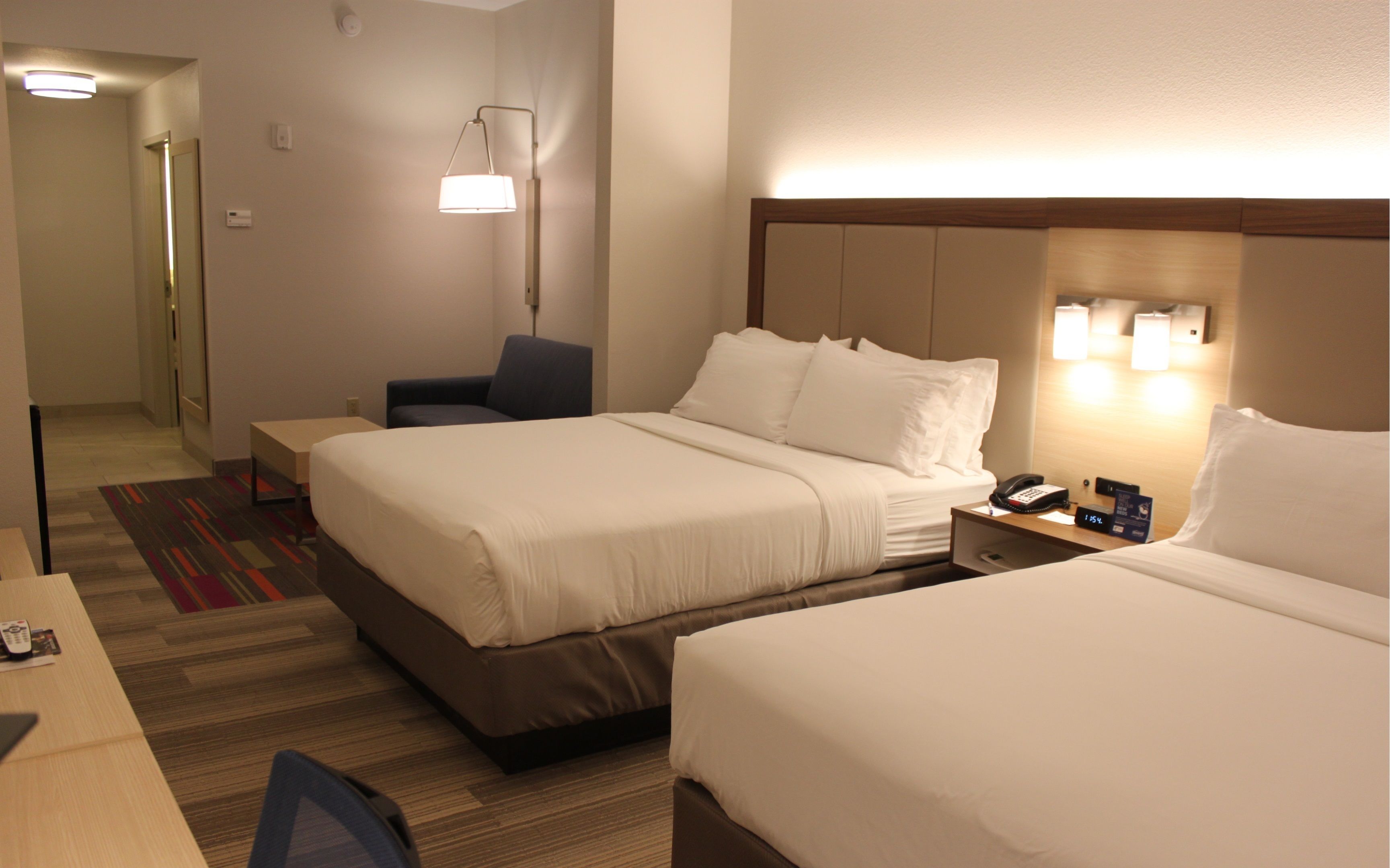A hotel room with two beds, a desk, a chair, a bedside table with a phone, and a lamp.