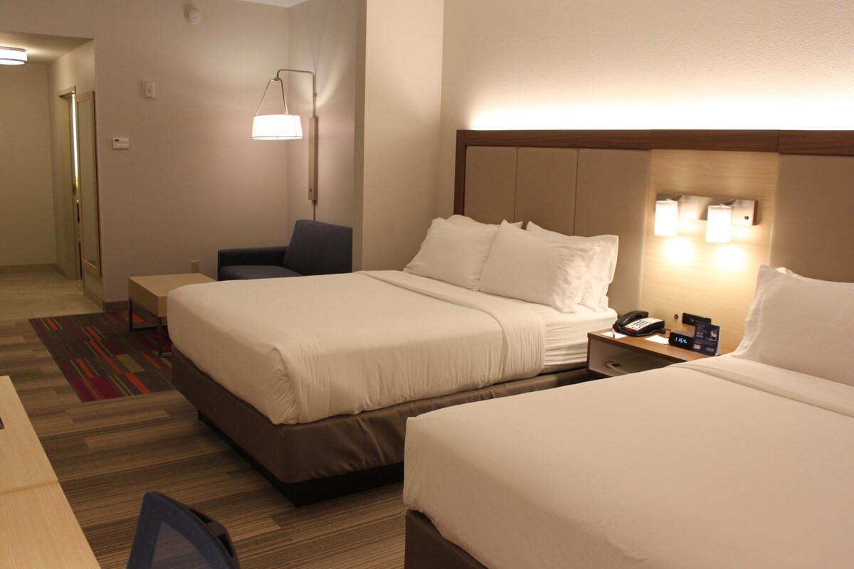 A hotel room with two beds, a desk, a chair, a bedside table with a phone, and a lamp.