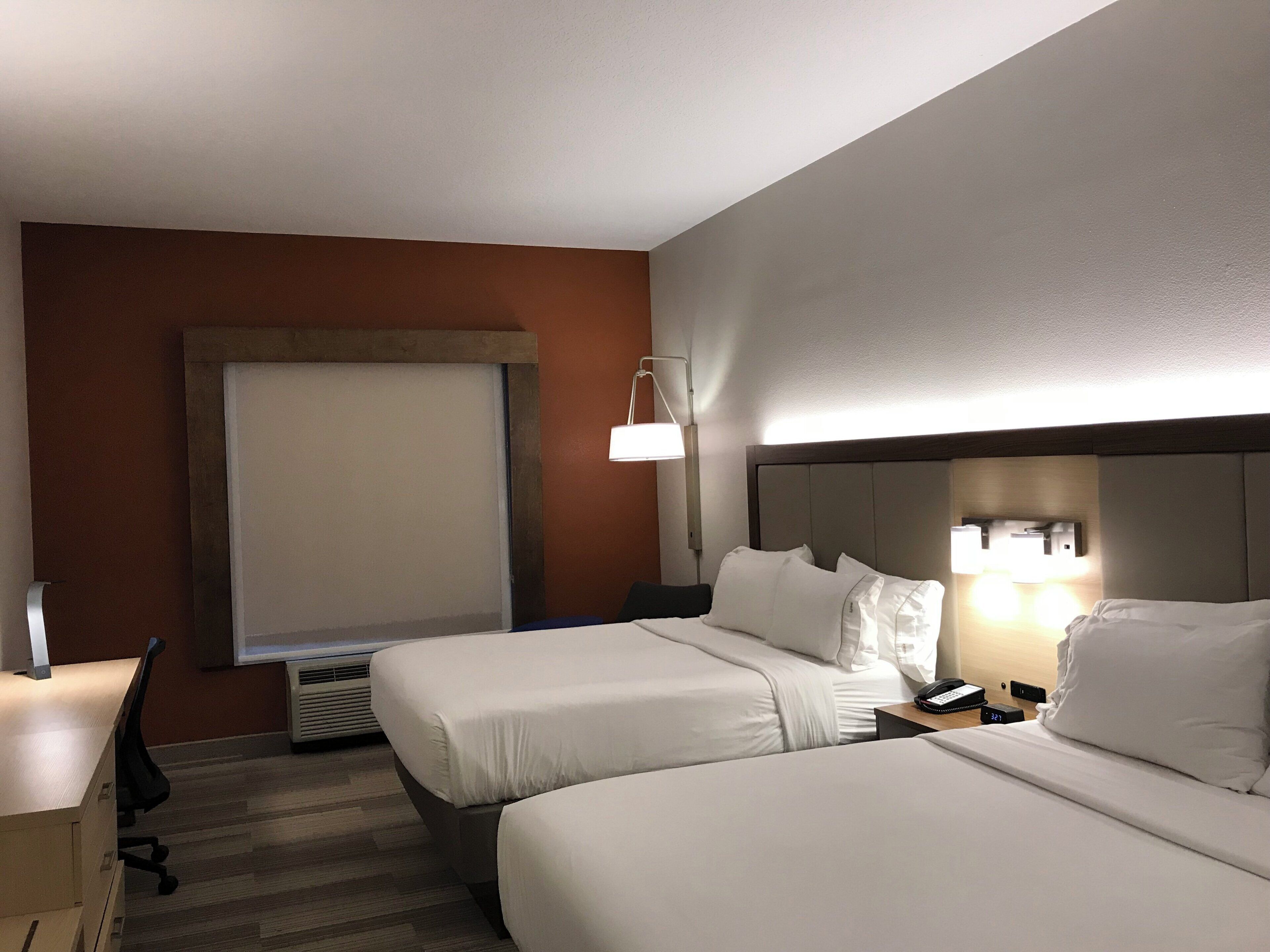 Une chambre d’hôtel avec deux lits, un bureau, une chaise, une lampe et une fenêtre.