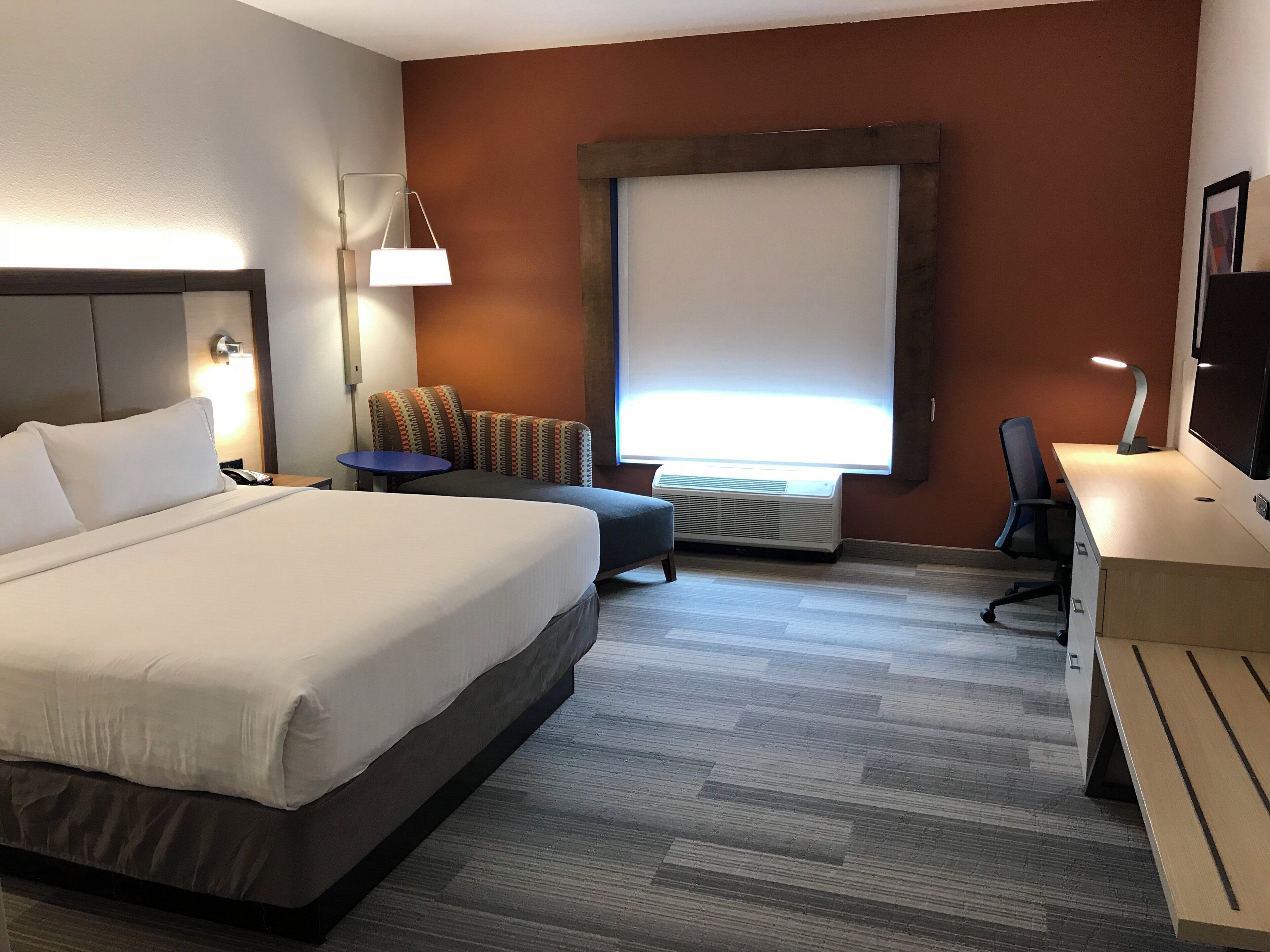 Una camera d'albergo con un letto, una scrivania, una sedia, un tavolino, una lampada e un'ampia finestra.