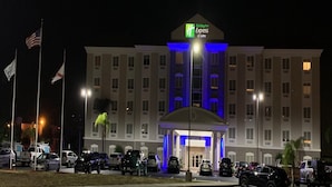 A Holiday Inn Express & Suites building at night with a prominent entrance and multiple flags. - Holiday Inn Express Hotel & Suites Orlando South-Davenport by IHG (Davenport)