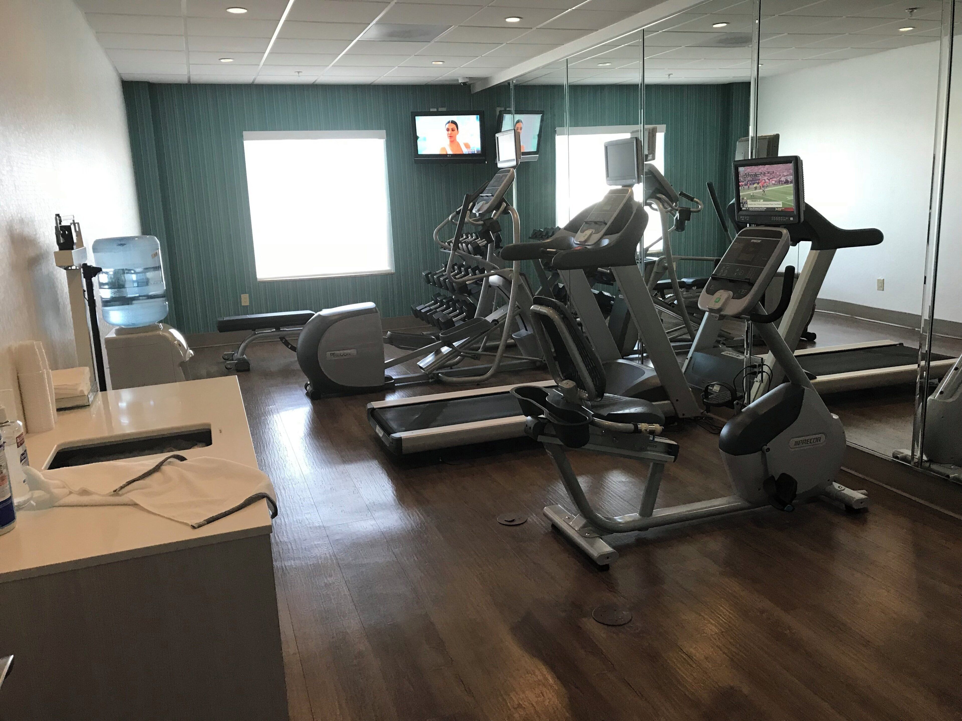 A gym with multiple treadmills, a water dispenser, and a mirror reflecting the room.