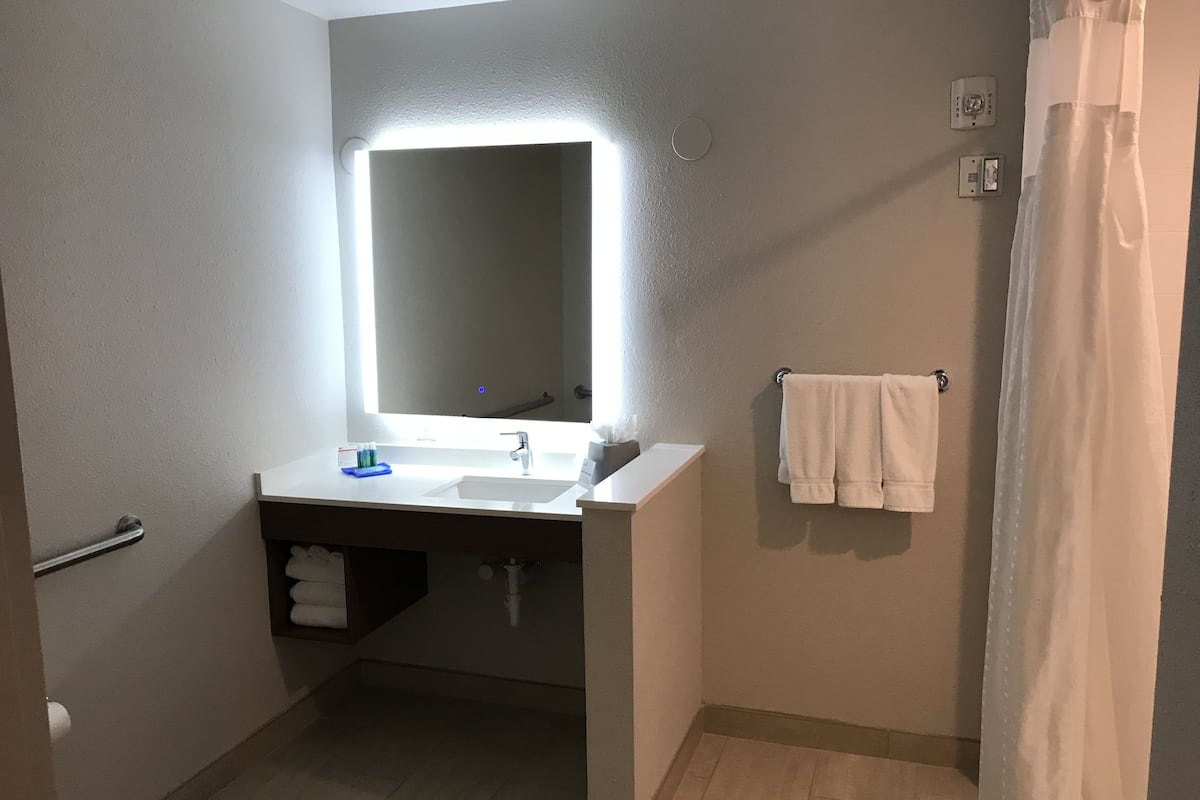 Ett badrum med ett vitt handfat, en spegel med inbyggd belysning, en handdukshängare och ett duschdraperi.