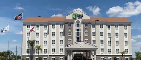 A multi-story hotel with a central entrance, flagpoles, and a clear sky.