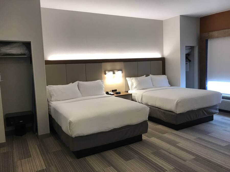 Una habitación de hotel con dos camas, una mesita de noche con lámpara, un armario y una ventana con persianas.