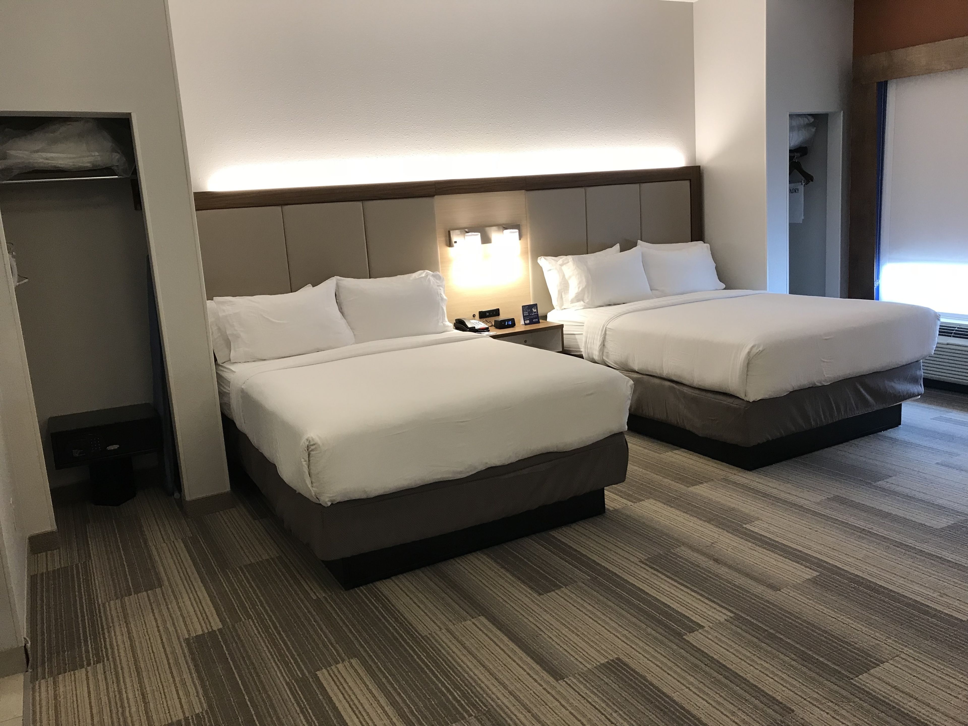 Habitación de hotel con dos camas, una mesita de noche con lámpara y un armario empotrado.