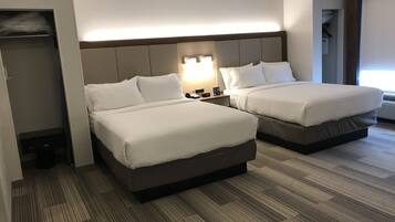 Habitación de hotel con dos camas, una mesita de noche con lámpara y un armario empotrado.