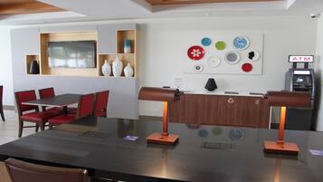 Un espace d’accueil comprenant un comptoir de réception, un coin salon avec des fauteuils rouges, un mur décoré d’assiettes et un distributeur automatique de billets.