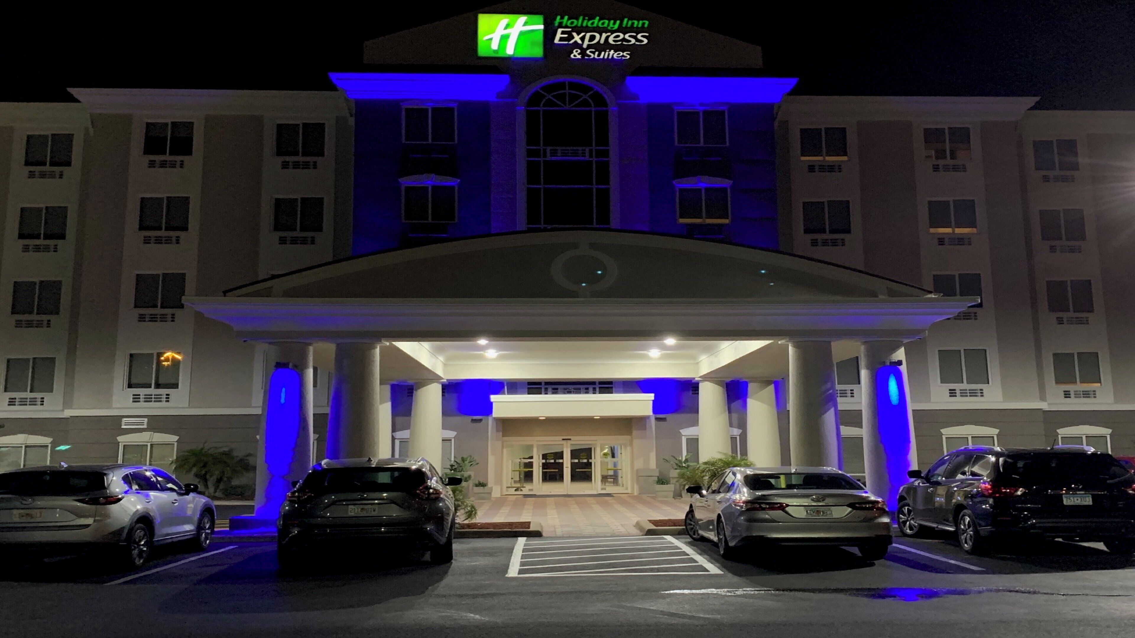 Edifício Holiday Inn Express & Suites com entrada coberta, vários carros estacionados em frente e vista clara para as portas de entrada.