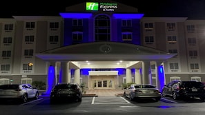 A Holiday Inn Express & Suites building with a covered entrance, multiple cars parked in front, and a clear view of the entrance doors. - Holiday Inn Express Hotel & Suites Orlando South-Davenport by IHG (Davenport)