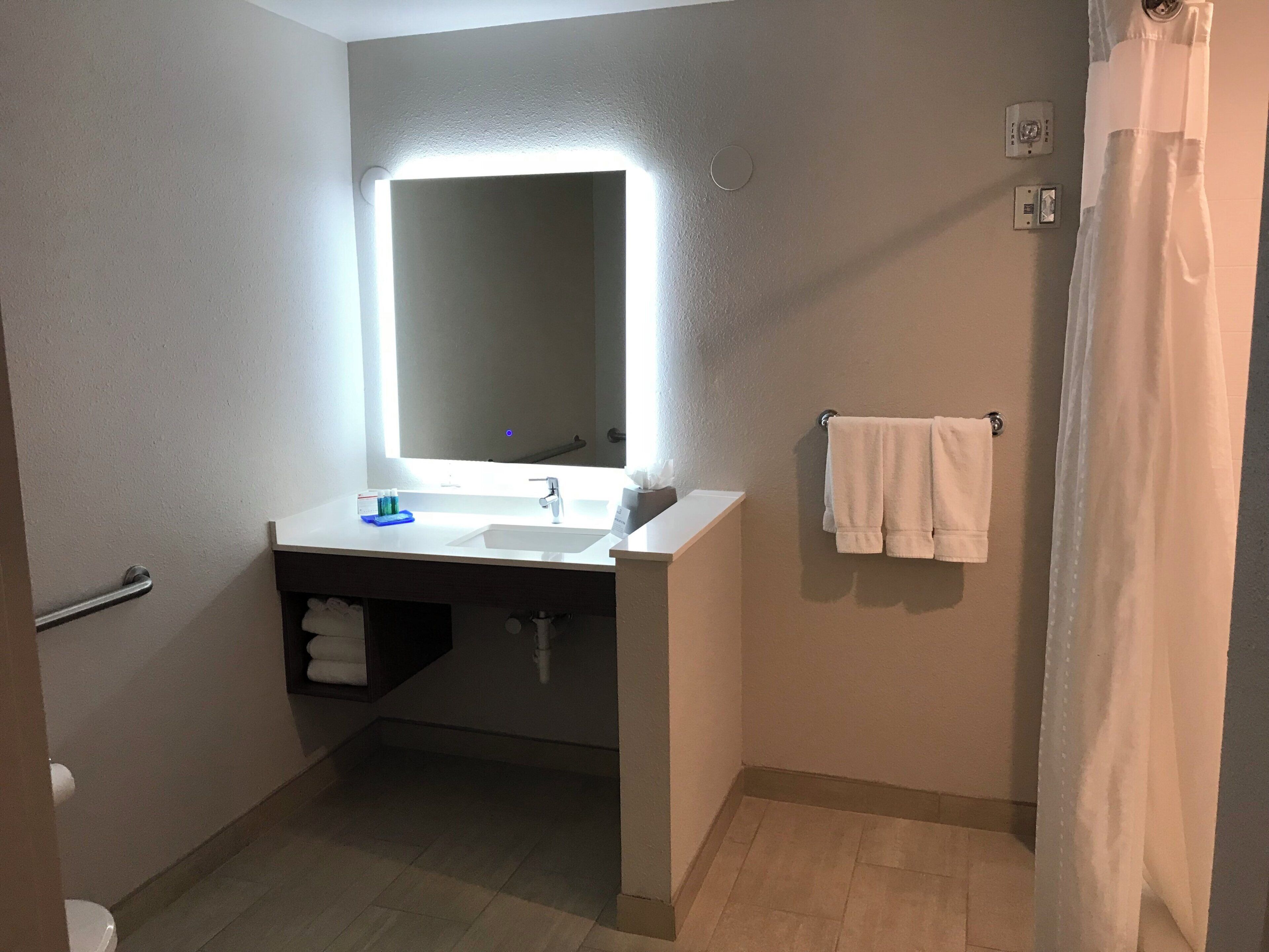 A bathroom with a white sink, a mirror with a light, a towel rack, and a shower curtain.