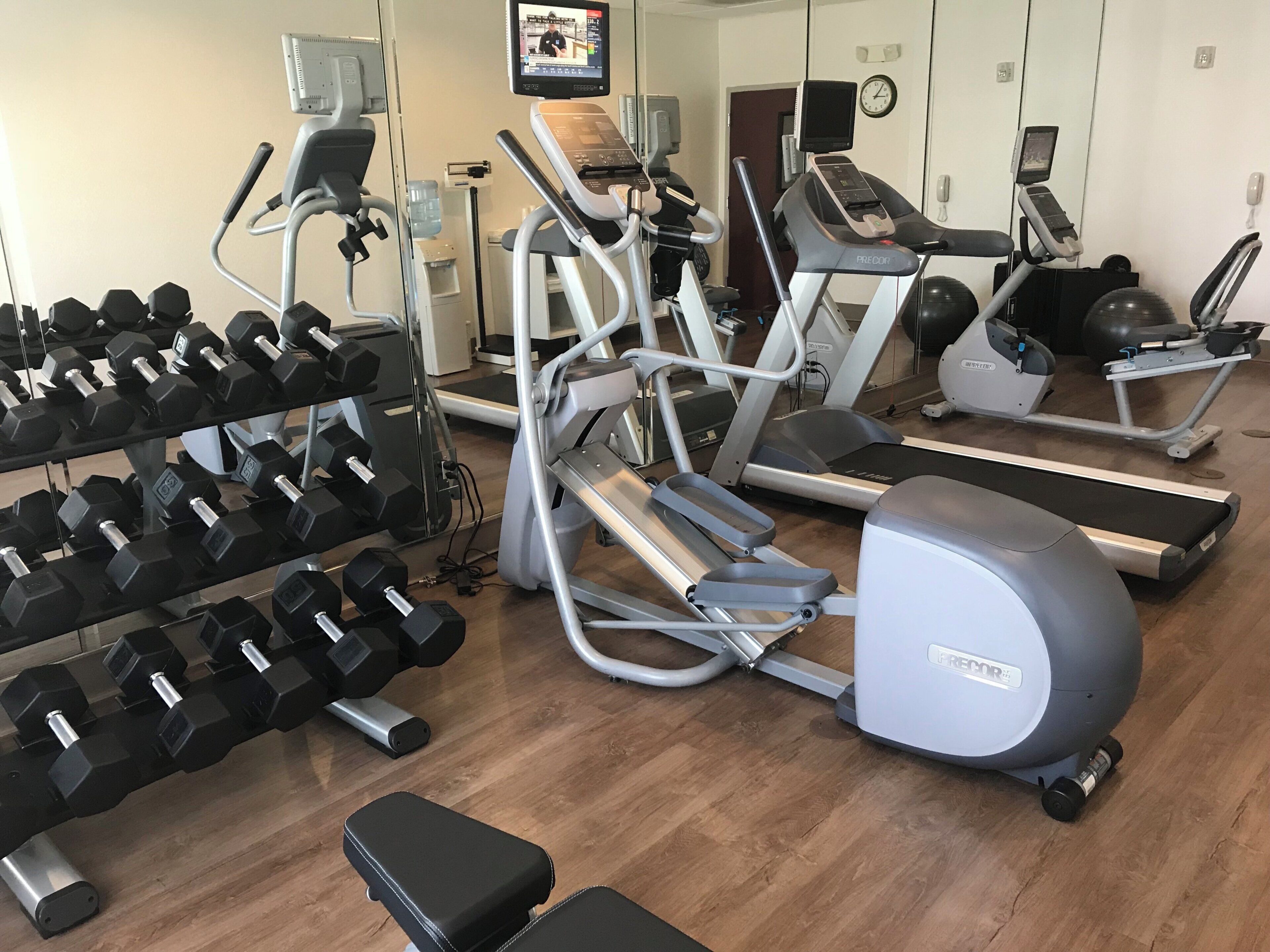 A gym with various exercise equipment including treadmills, elliptical machines, and dumbbells.