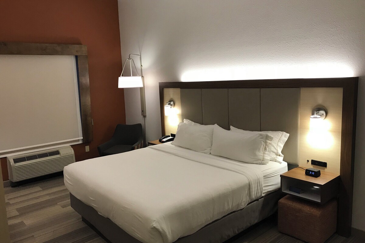 A hotel room with a bed, bedside tables, a chair, a lamp, and a wall-mounted light fixture.
