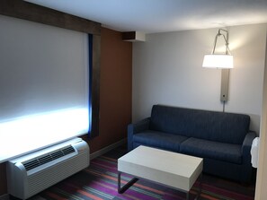 A modern hotel room with a large window, a blue sofa, a white coffee table, and a standing lamp. - Holiday Inn Express Hotel & Suites Orlando South-Davenport by IHG (Davenport)