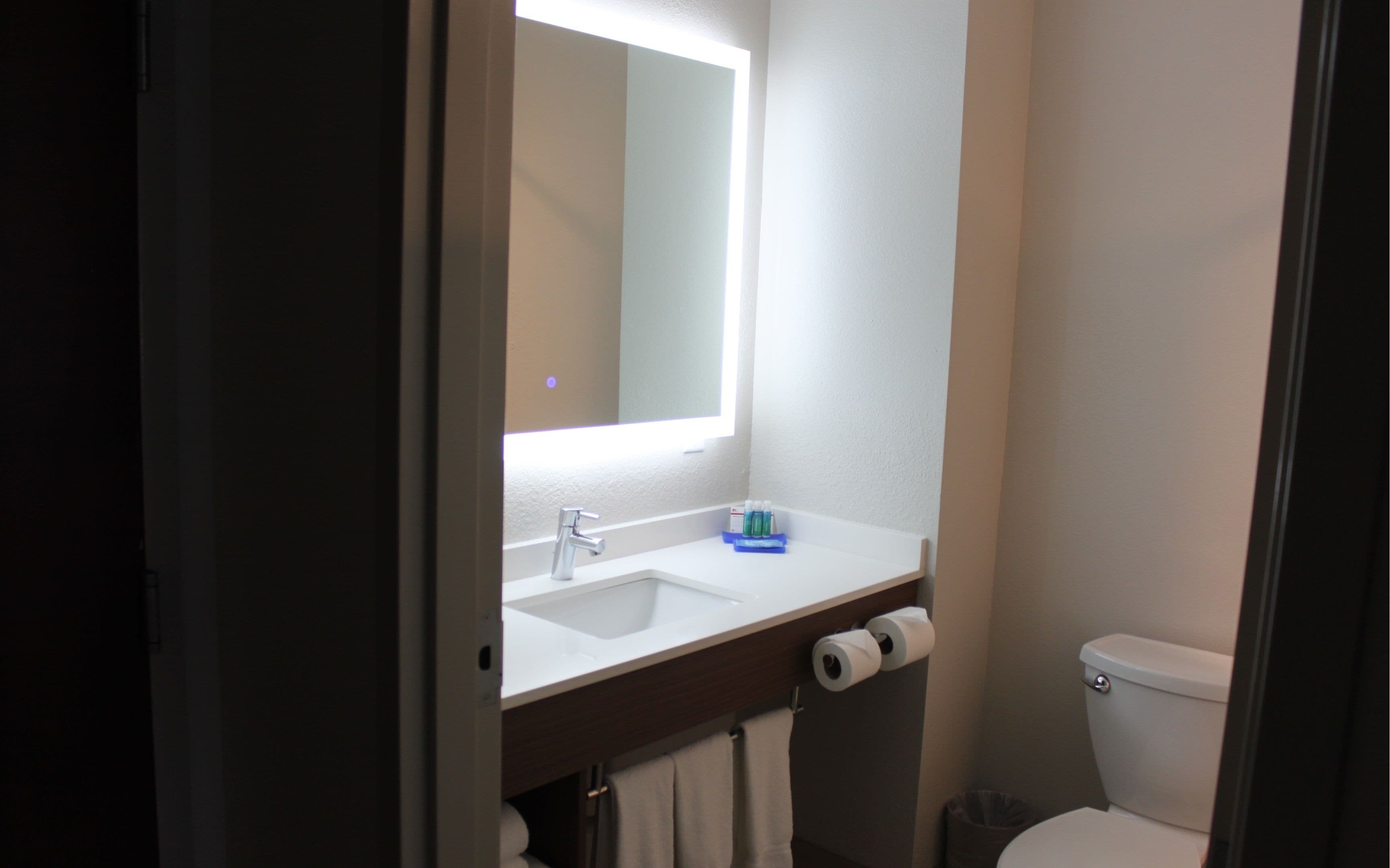 Une salle de bain avec un lavabo blanc, un miroir, des toilettes et un rouleau de papier toilette.