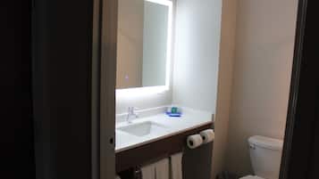 Un baño con un lavamanos blanco, un espejo, un inodoro y un cubo de basura.