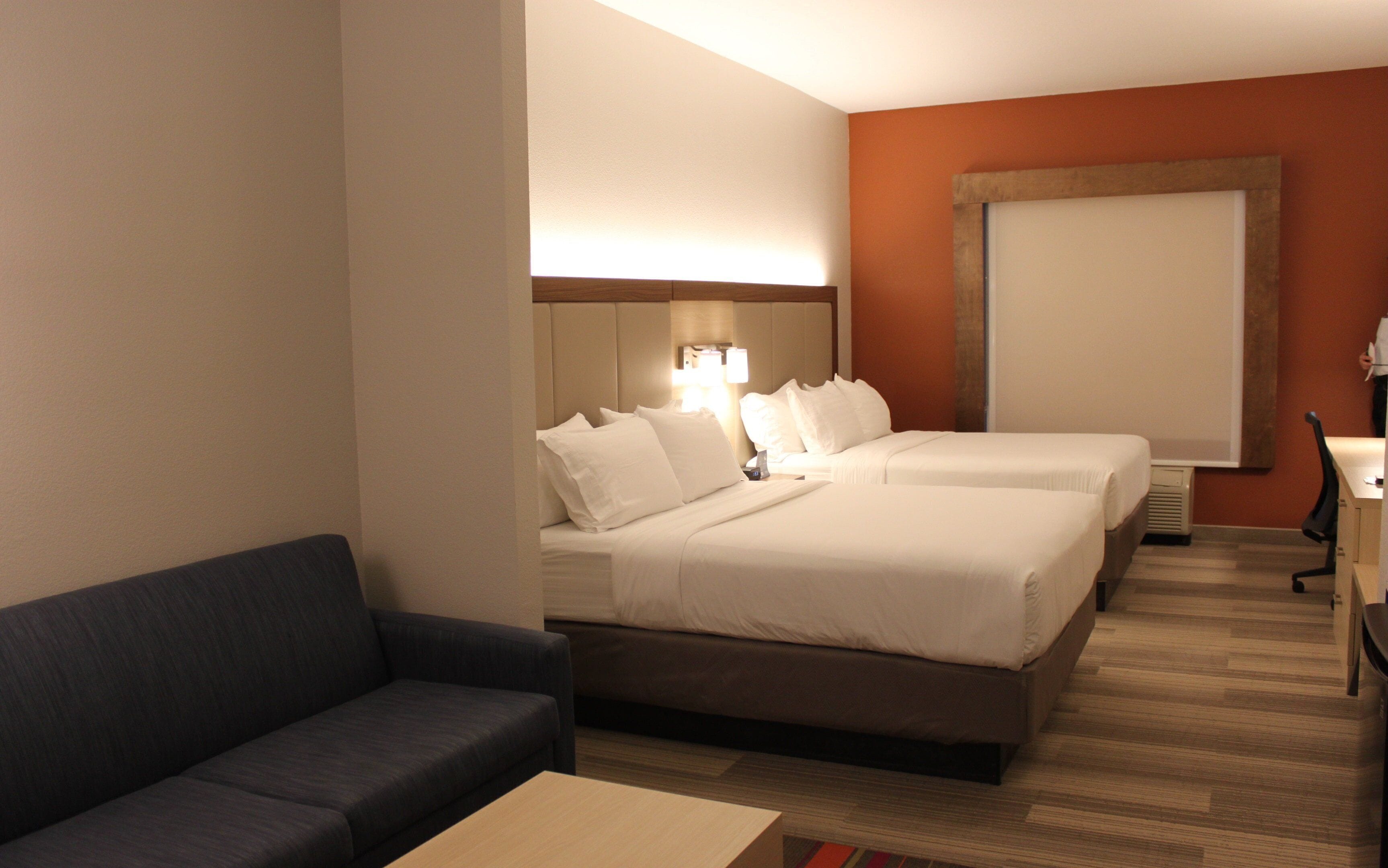 A hotel room with two beds, a sofa, a desk, and a large window.