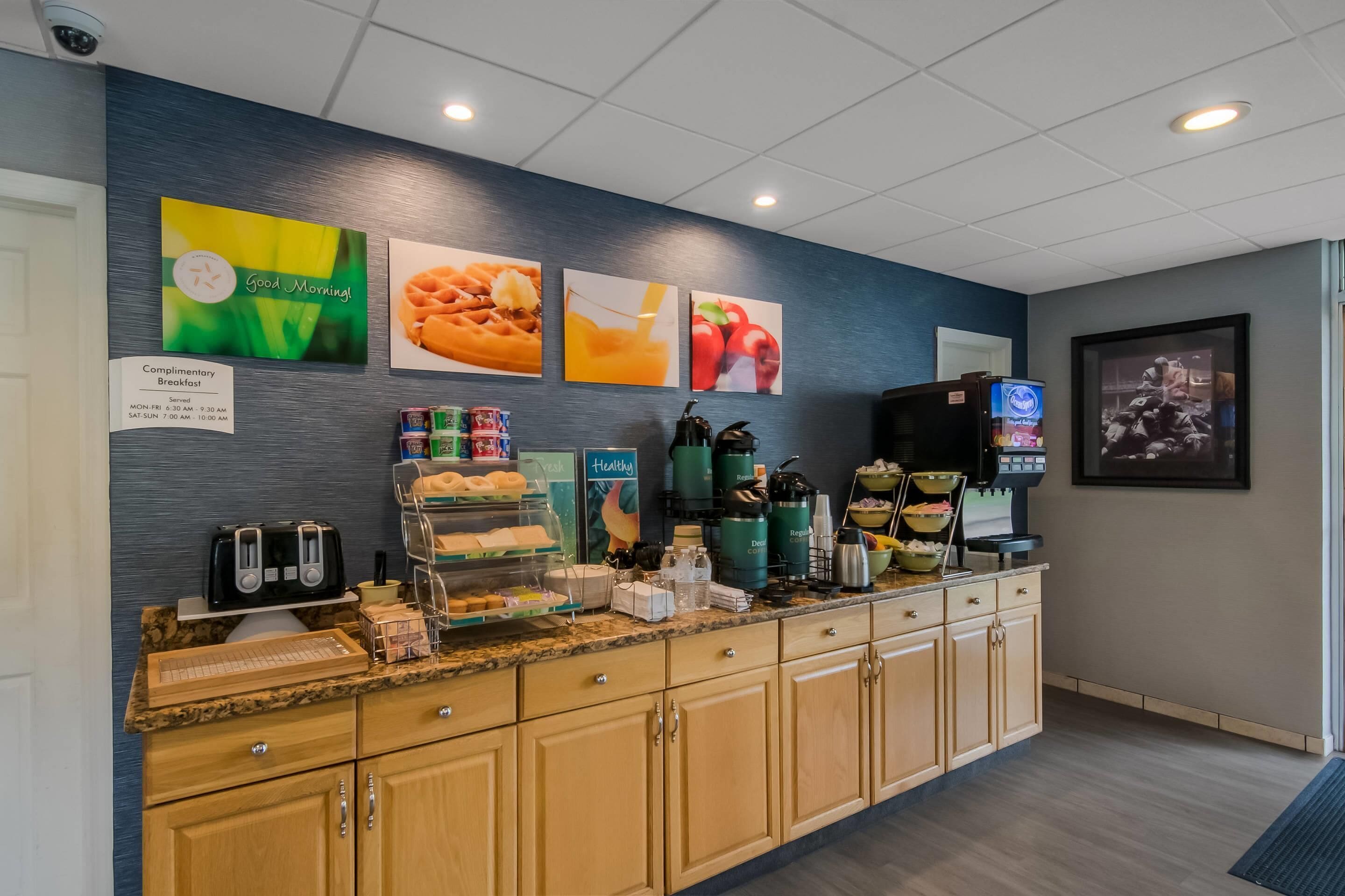 Zona de desayuno de hotel con un mostrador que exhibe alimentos, una máquina de café y un letrero que anuncia desayuno gratuito.