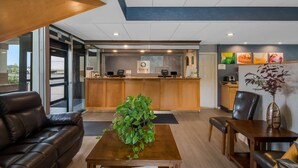 A modern hotel lobby with a reception desk, a coffee machine, a plant, a leather sofa, and a dining area.