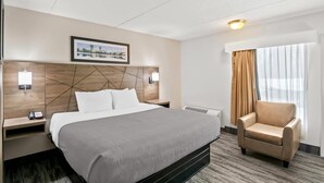 A hotel room with a large bed, a chair, a nightstand with a phone, a wall-mounted light, and a window with curtains.