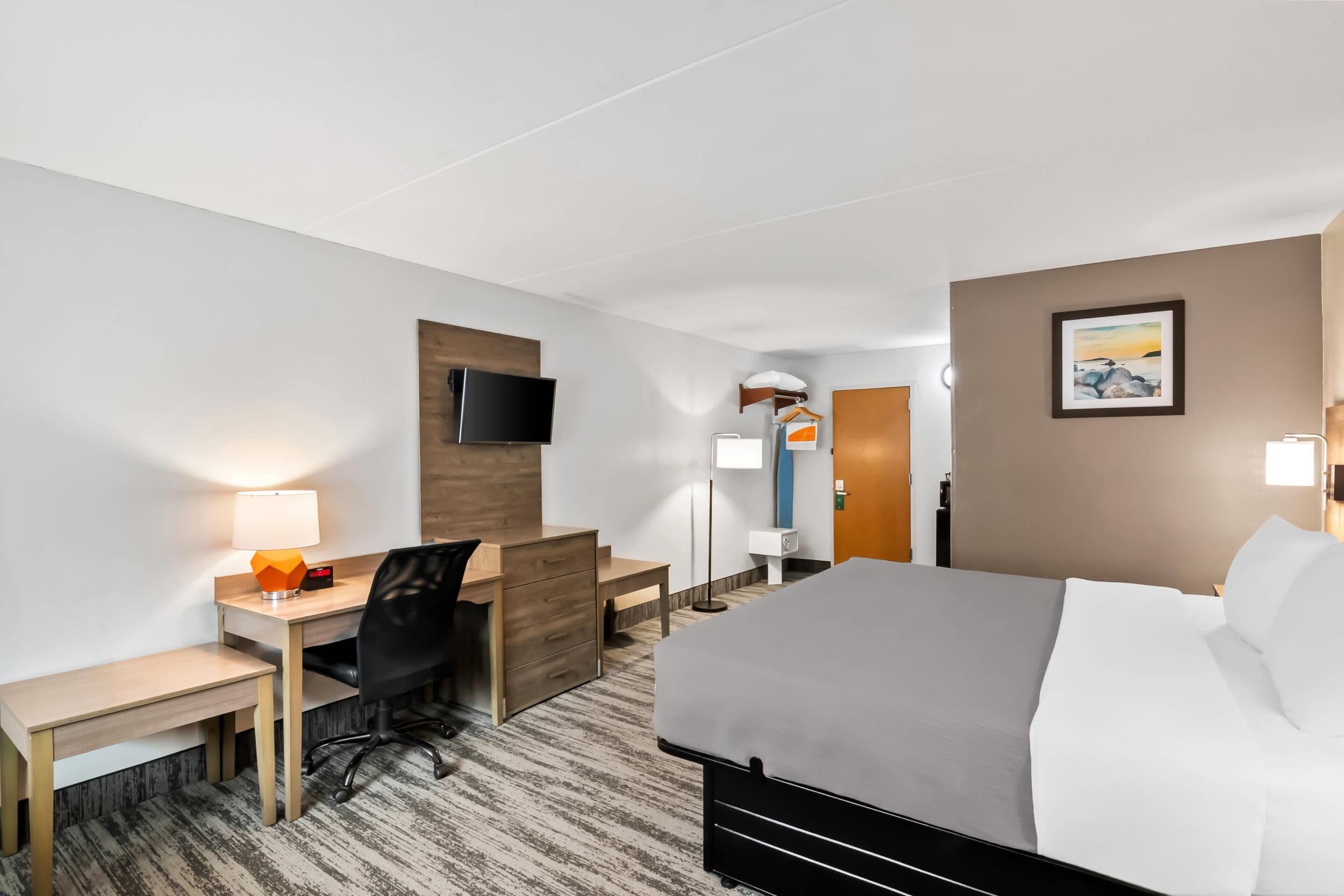 Una habitación de hotel con cama, escritorio, silla y televisor en la pared.
