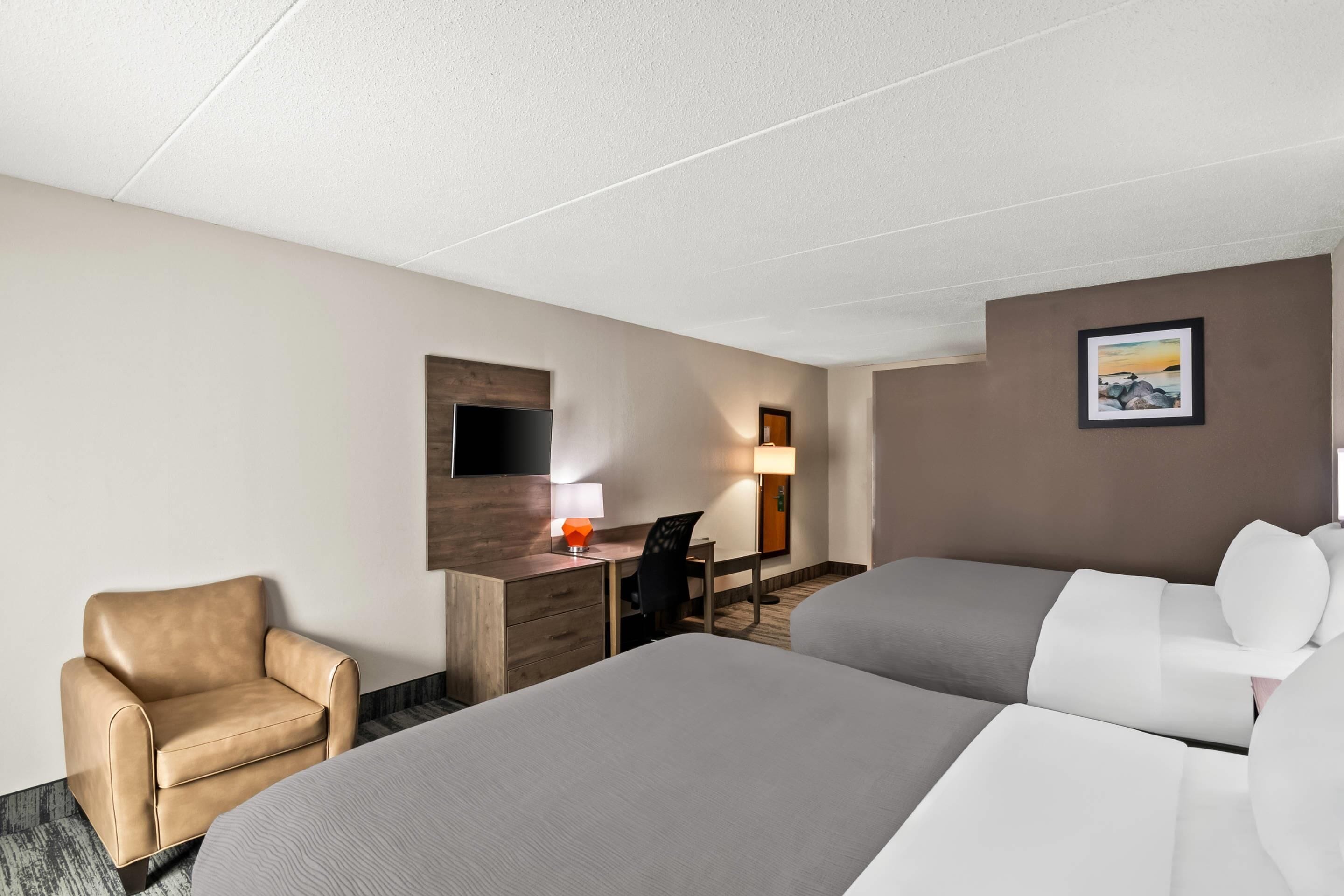 A hotel room with two beds, a desk with a chair, a TV, and a painting on the wall.