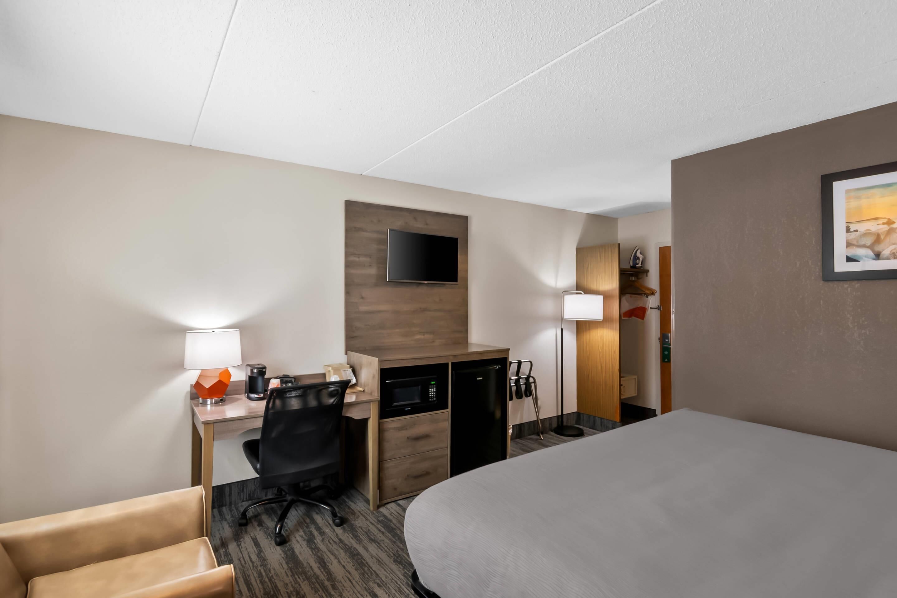 Habitación de hotel con cama, escritorio, silla y televisor montado en la pared.