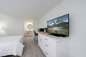 A bedroom with a bed, a TV on a white dresser, a microwave, and a chair. - Varsity South (Centralia)