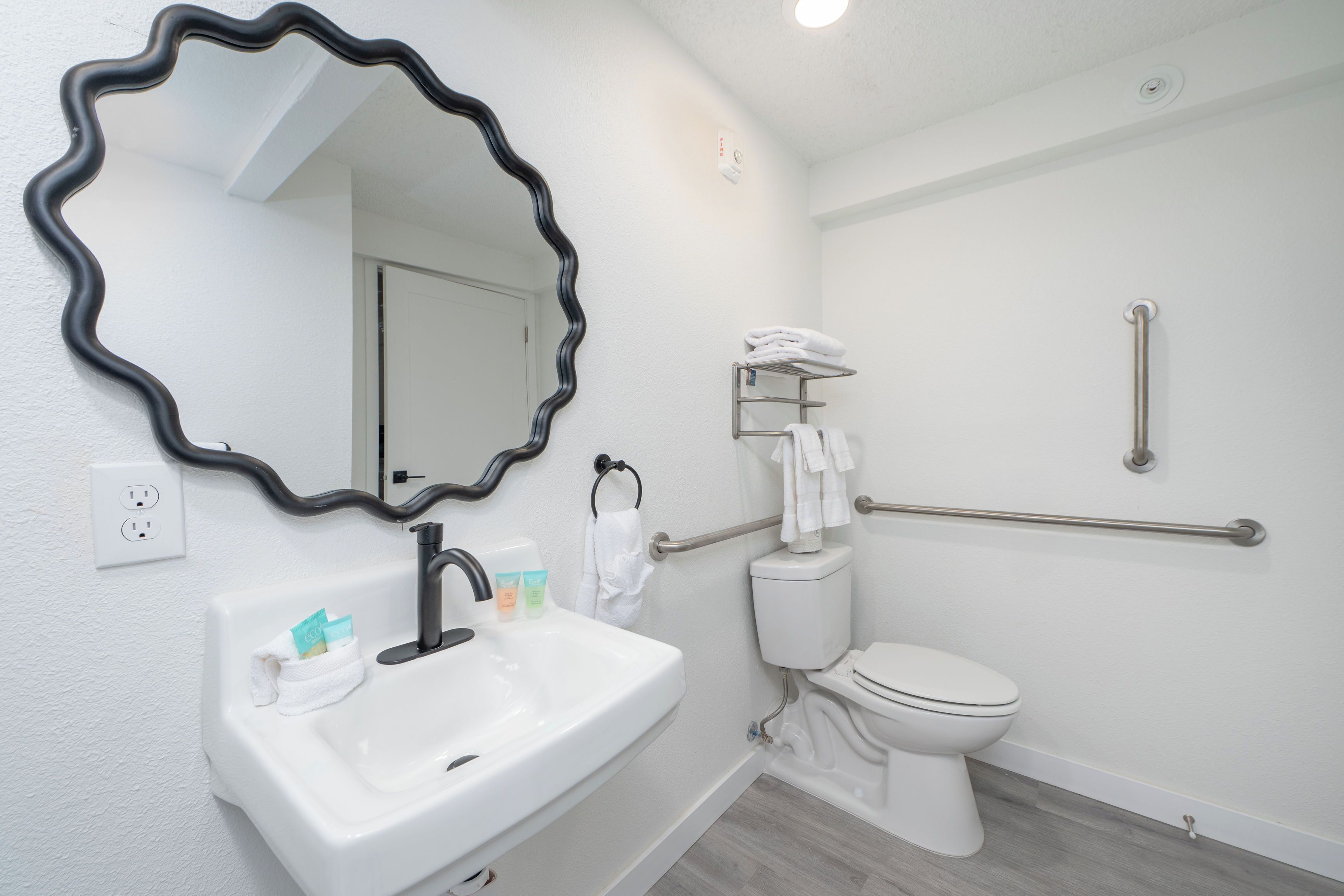 A bathroom with a white sink, a mirror, a toilet, and a grab bar.