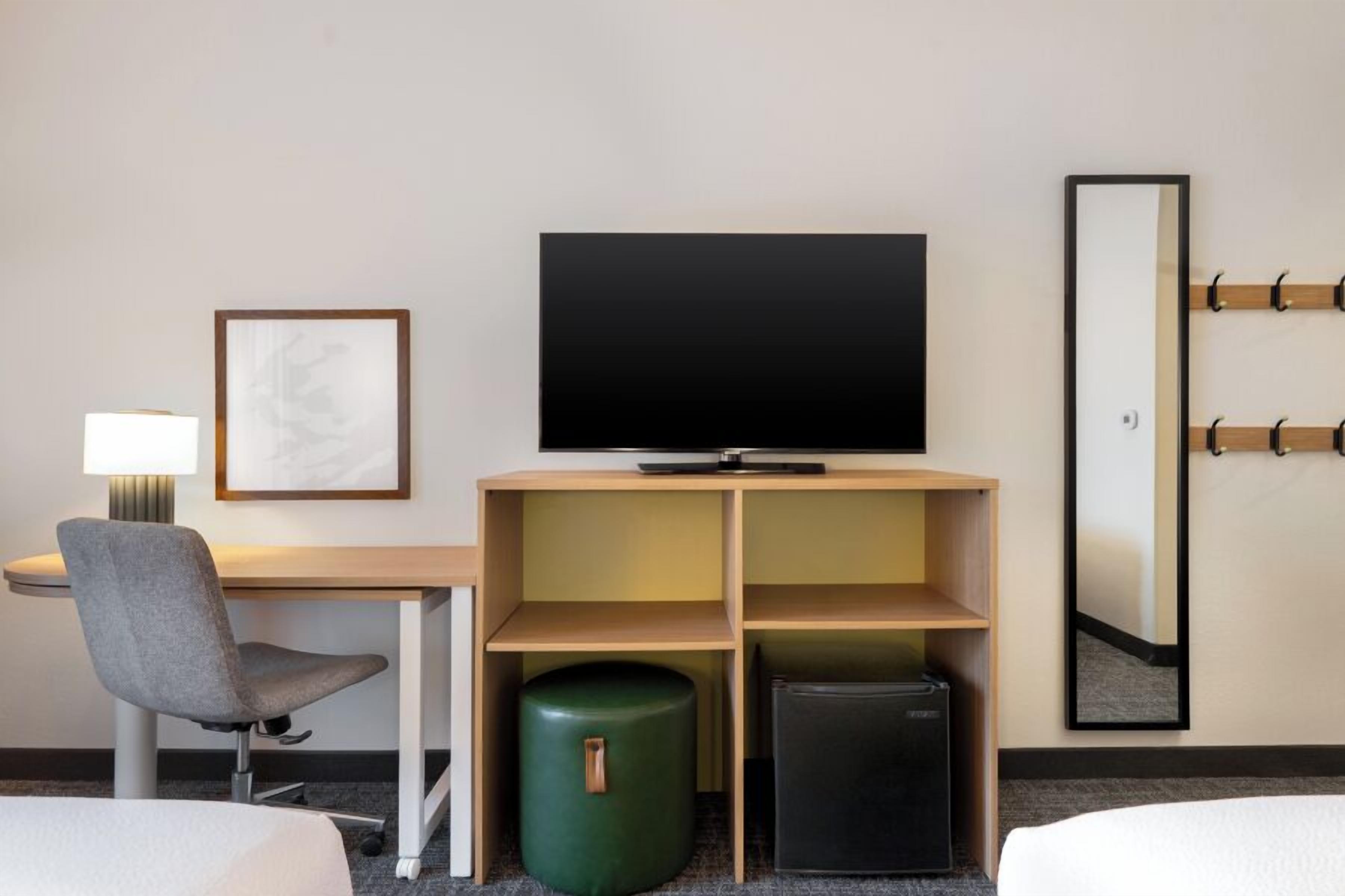 A hotel room with a desk, chair, television, and a bed.