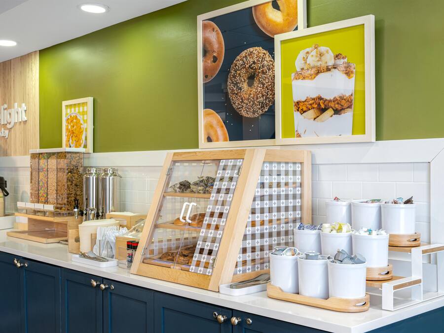 A breakfast bar with a coffee machine, a framed picture of pastries, and a display of food items.