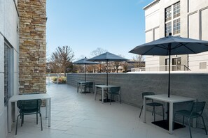 An outdoor patio area with tables and chairs, umbrellas, and a stone wall. - Spark by Hilton Murfreesboro (Murfreesboro)