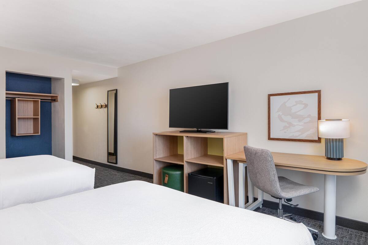 A hotel room with a bed, a desk with a computer, a TV, a lamp, and a framed picture on the wall.