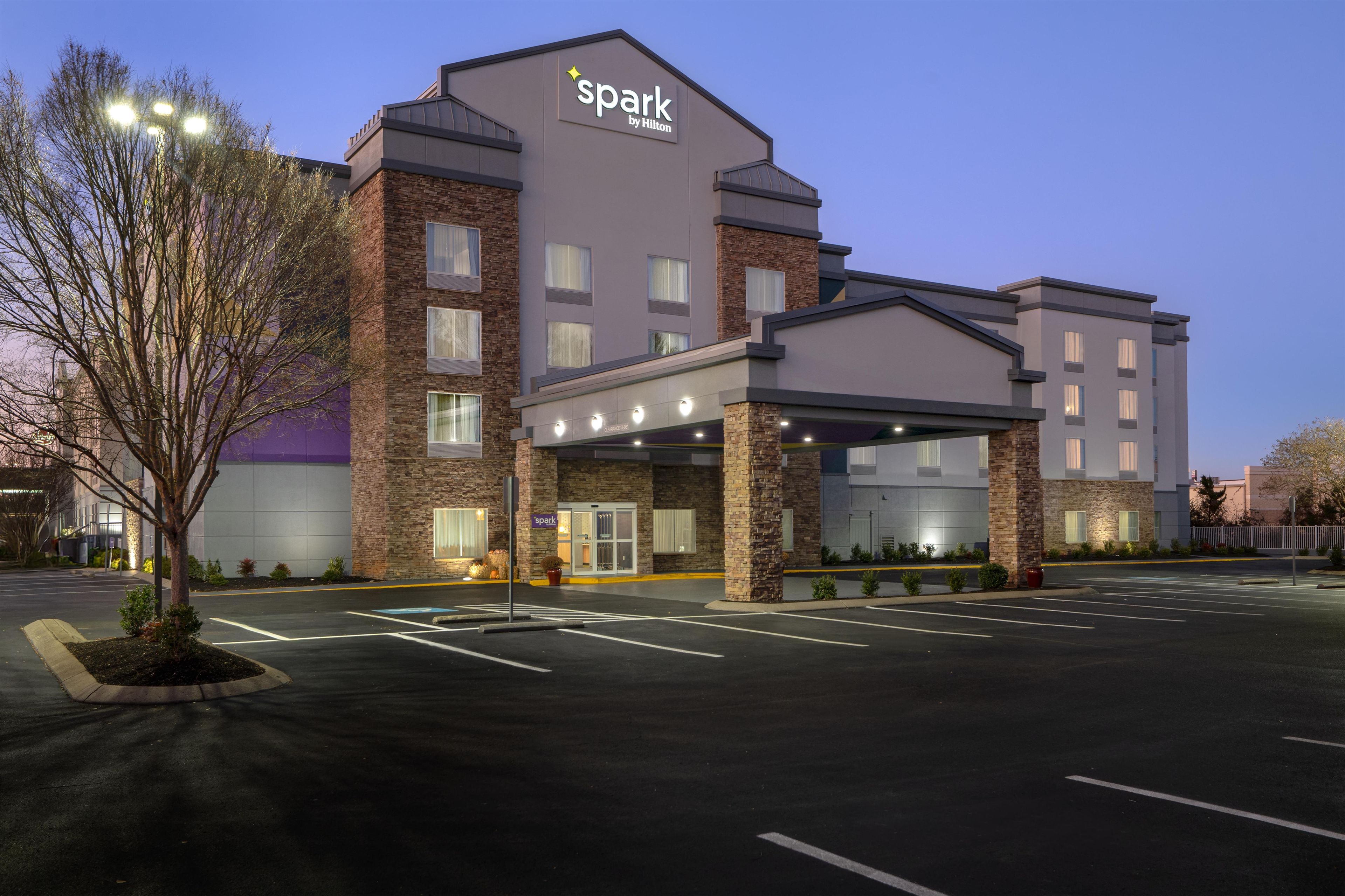 A hotel with a modern design, featuring a prominent 'spark by Hilton' sign, a covered entrance, and a parking lot.