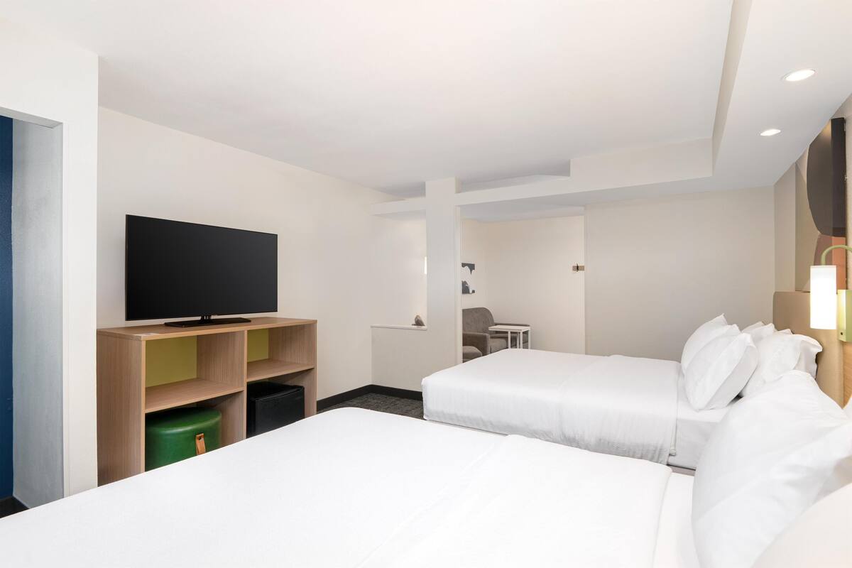 A hotel room with two beds, a TV on a wooden shelf, a desk, and a chair.
