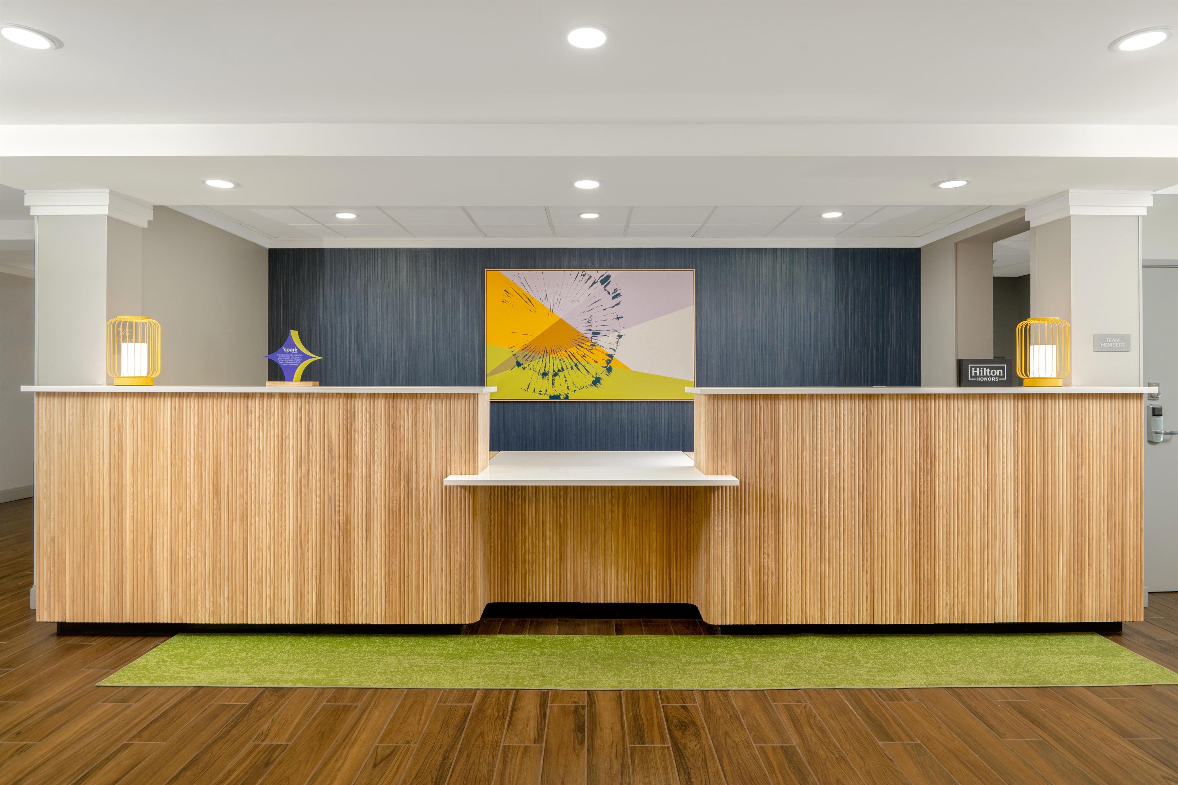 A reception desk with a wooden finish, a green carpet, and a wall-mounted artwork.