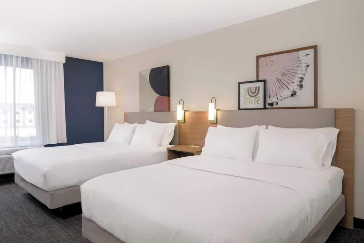 A hotel room with two beds, a nightstand with a lamp, and artwork on the wall.