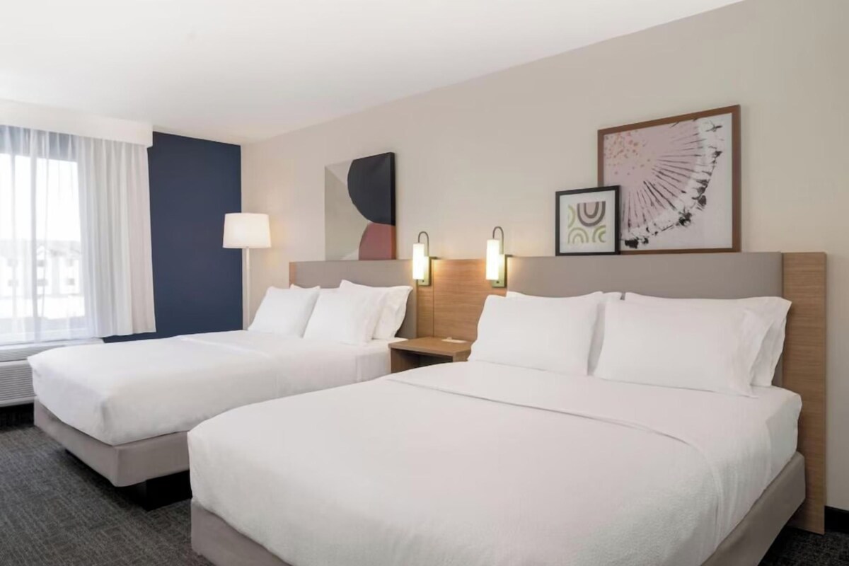 A hotel room with two beds, a nightstand with a lamp, and artwork on the wall.