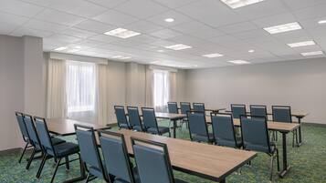 A conference room with multiple tables and chairs, large windows with curtains, and a carpeted floor.